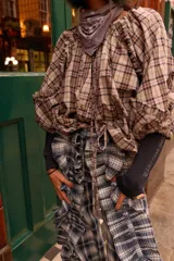 Camisa de manga larga con estampado a cuadros en tonos beige, marrón y azul. Presenta volados en las mangas, botones a la vista, puños elásticos y tiritas ajustables en el dobladillo para entallar.