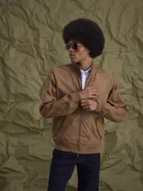 Campera tipo bomber color marrón, confeccionada en tela encerada, con cierre frontal, cuello tipo mao y puños y ruedo acanalados.