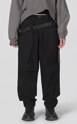Pantalón de estilo utilitario oversize confeccionado en tejido técnico ripstop. Presenta cintura elástica con broche tipo mochilero, bolsillos cargo frontales de gran tamaño con cierre, bolsillos traseros tipo ojal y sistema de ajuste en los tobillos mediante broches a presión.