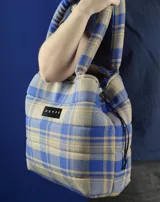 Bolso tipo tote bag de franela a cuadros en tonos azul y beige, con asas tubulares acolchadas y cierre con cordón ajustable.