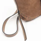 Cartera de gamuza color marrón con detalles de tachas metálicas en los laterales inferiores. Presenta una correa central vertical con hebilla decorativa en tono beige y correa larga ajustable para llevar al hombro o cruzada.