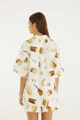 Camisa oversize blanca con estampado de instrumentos musicales, cuello camisero, botones frontales, hombros caídos y mangas cortas amplias.