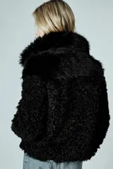 Abrigo corto de Zara Woman Collection con cuello de solapa y manga larga. Presenta una combinación de texturas con aplicación de pelo sintético y diseño de efecto rizado en mangas y bordes. Cuenta con forro interior y cierre frontal mediante ganchos metálicos.