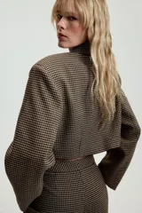 Blazer corta de corte recto con estampado de cuadros pequeños en tonos marrones y negros. Presenta cuello solapa, manga larga y cierre frontal con un botón.
