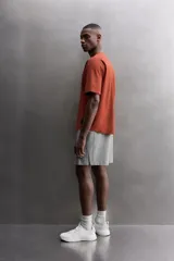 Camiseta de ajuste relajado (relaxed fit) color terracota, confeccionada en tejido técnico. Presenta cuello redondo, mangas ranglán cortas y un parche negro con logo en el bajo.