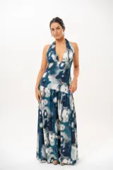 Vestido largo con escote halter profundo y diseño sin mangas. Presenta un estampado difuminado en tonos azules, celestes, blancos y grises, con corte ajustado en el torso y una falda larga con vuelo.