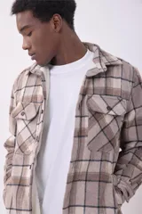 Sobrecamisa de corte holgado con diseño a cuadros en tonos beige y marrón, confeccionada en tejido de textura suave. Presenta cuello clásico, cierre frontal con botones, dos bolsillos con solapa en el pecho y puños abotonados.
