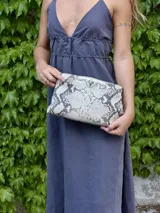 Mini cartera tipo sobre color arena con textura de reptil, cierre metálico dorado y cadena fina dorada para llevar al hombro.