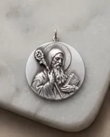 Dije circular de alpaca con diseño de San Benito en relieve, con acabado envejecido y diseño reversible.