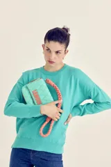 Cartera tipo bandolera acolchada color turquesa, con correa trenzada color salmón y logo bordado en el frente.