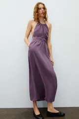 Vestido midi de color morado con cuello halter, tirantes finos ajustables y espalda descubierta. Cuenta con detalles fruncidos en el delantero y la cintura.