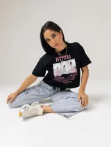 Remera crop negra de algodón con estampa frontal inspirada en el álbum Futttura de Tini, que incluye fotografías tipo polaroid y lista de canciones en color rosado. Presenta cuello redondo, mangas cortas y parche con logos de Under Armour y Tini en el ruedo.
