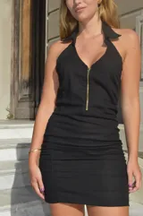 Vestido corto negro con escote halter y cierre frontal con cremallera dorada.