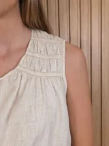 Musculosa de lino color blanco, de corte holgado, con cuello en V, detalles de tablas y frunces en los hombros, y dobladillo desflecado.