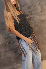 Musculosa tejida en punto calado color negro con destellos brillantes, presenta un diseño de flecos largos en el ruedo que combinan tonos rojizos, dorados y oscuros.