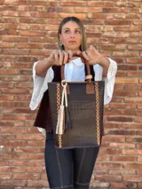 Bolso matero de cuero color chocolate con textura croco, asas cortas y detalle de costuras en los laterales. Incluye un dije con flecos en tonos beige y negro.