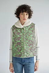 Chaleco de denim con estampado botánico en tonos verde y marrón, con interior de corderito sintético y cuello solapa. Presenta cierre frontal con botones y dos bolsillos delanteros.