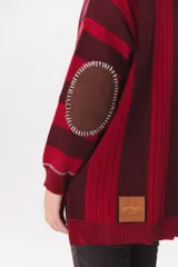 Buzo de tejido de punto con diseño de rayas verticales en tonos bordó y rojo. Presenta cuello alto con cierre frontal, mangas largas con coderas en contraste y detalles de costuras visibles.