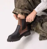 Botas estilo Chelsea de cuero color marrón, con paneles elásticos laterales negros, presillas traseras y suela chunky de goma negra con plataforma dentada.