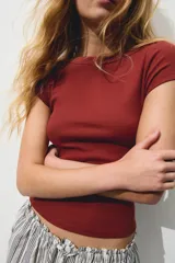 Top corto ajustado de punto acanalado color terracota, con mangas cortas y escote bote con detalle de solapa en los hombros.