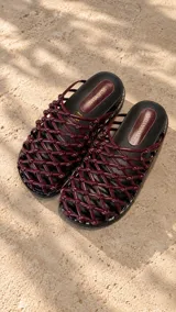 Sandalias planas de cuero color bordó, con diseño de tiras entrelazadas en forma de red y nudos. Cuentan con suela plana y plantilla acolchada.