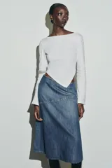 Camiseta de cuello barco y manga larga con diseño asimétrico en el bajo. Presenta un corte entallado con cierre lateral mediante cremallera oculta.