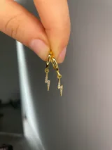 Aros argollas dorados con dijes colgantes en forma de rayo incrustados con circonias.