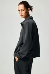 Buzo en tejido liviano color gris oscuro, con cuello camisero, tapeta de botones, hombros caídos y puños acanalados.