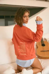 Buzo color naranja con cuello redondo, manga larga y un pequeño corazón bordado en el frente. La espalda presenta un bordado con el significado de "Munay" y un poema. Confeccionado en rústico de algodón.