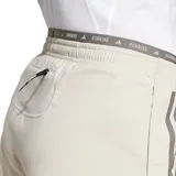 Short de running color crema con cintura elástica gris con la inscripción "Running" repetida. Presenta tres tiras grises a los costados y logo de Adidas en el ruedo.