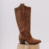 Bota texana de cuero color suela, con taco cuadrado y puntera fina. Presenta costuras decorativas en contraste a lo largo de la caña y en la parte frontal.