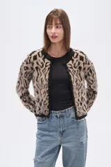 Cardigan de tejido de punto, corto, con estampado animal print en tonos beige y negro. Presenta cuello redondo y ribetes negros en el borde frontal, puños y ruedo.