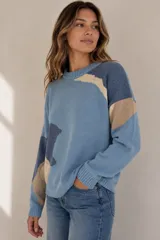 Buzo de punto color beige con diseño geométrico y abstracto en tonos rojo, azul y marrón, de corte holgado, cuello redondo y mangas largas.