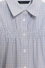 Camisa de algodón con estampado de cuadros, cuello solapa, mangas cortas abullonadas y detalle de fruncido elástico en el pecho. Cierre frontal con botones.