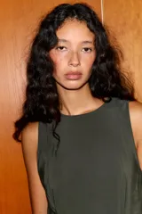 Vestido midi color verde oscuro, confeccionado en tejido fluido. Presenta cuello redondo, manga sisa y bajo con línea evasé y pliegues. Tiene cierre lateral con cremallera oculta y cierre en la espalda con abertura y botón.