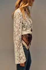 Top de encaje negro con cuello redondo, manga larga y hombreras incorporadas. Presenta un diseño de corte recto y cierre posterior.