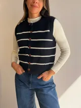 Chaleco tejido de punto con diseño de rayas horizontales en color negro y blanco. Presenta cuello redondo, cierre frontal con botones y terminaciones en tejido acanalado.