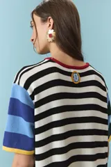 Vestido midi de algodón con diseño de rayas horizontales en color blanco y negro en el torso, mangas cortas con bloques de colores celeste, azul, verde y amarillo, y parte inferior con franjas anchas en rojo, amarillo y azul. Cuenta con cuello redondo ribeteado en rojo.