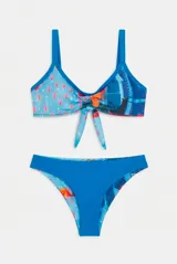 Conjunto de bikini de dos piezas con estampado floral en tonos rojo, violeta y verde sobre fondo claro, con detalles en color amarillo en los bordes y tirantes. El corpiño es de estilo deportivo con tiras para anudar al frente, y la bombacha es de corte clásico.