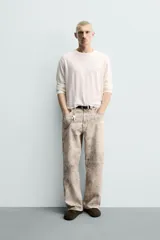 Pantalón de corte baggy fit confeccionado en tejido de algodón con efecto lavado y estampado abstracto en tonos beige y gris. Presenta diseño de cinco bolsillos, cierre frontal con cremallera y botón.