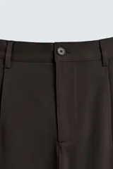 Pantalón de corte recto confeccionado en tejido elástico, con cintura elástica, pliegues frontales, bolsillos laterales y bolsillos traseros de vivo con botón.