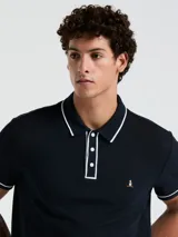 Polo de piqué azul marino con vivos blancos en cuello y mangas, calce slim fit y logo bordado en el pecho.