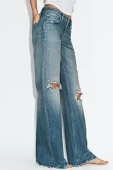 Jeans de tiro medio con diseño flare, efecto lavado y detalles de roturas en las piernas. Presenta cinco bolsillos, trabillas para cinturón y bajo deshilachado sin costuras.