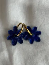 Aros de argolla dorada con dije colgante en forma de flor de acrílico azul con acabado brillante.