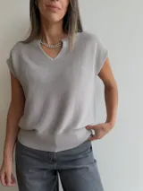 Tejido de punto de manga corta con escote en V, que incluye una cadena decorativa desmontable con apliques brillantes. Presenta un diseño holgado con terminación de puño elástico en la cintura.