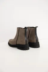 Bota corta de cuero color visón, con diseño de costuras visibles en la puntera y cierre lateral. Presenta una suela plana de goma negra.