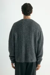 Saco gris de punto trenzado con escote en V pronunciado y botones frontales. Presenta remate acanalado en cuello, tapeta, puños y bajo. Corte holgado.