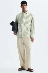 Camisa de popelina de algodón con cuello inglés, tapeta clásica, bolsillo superior abierto y canesú con pliegue en la espalda. Cuenta con mangas largas, puños ajustables con botón y bajo ligeramente redondeado. Presenta un diseño de rayas verticales en tonos verde y blanco.