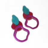 Par de aros colgantes con diseño abstracto en acrílico. Presentan una pieza superior con forma irregular en color turquesa con glitter y una pieza inferior con forma de aro irregular en color fucsia metalizado.