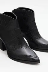 Bota corta estilo western de cuero vacuno negro, con puntera fina y detalles de textura grabada tipo reptil. Presenta costuras decorativas y apliques de tachas metálicas pequeñas en el diseño. Cuenta con taco cuadrado y cierre lateral.
